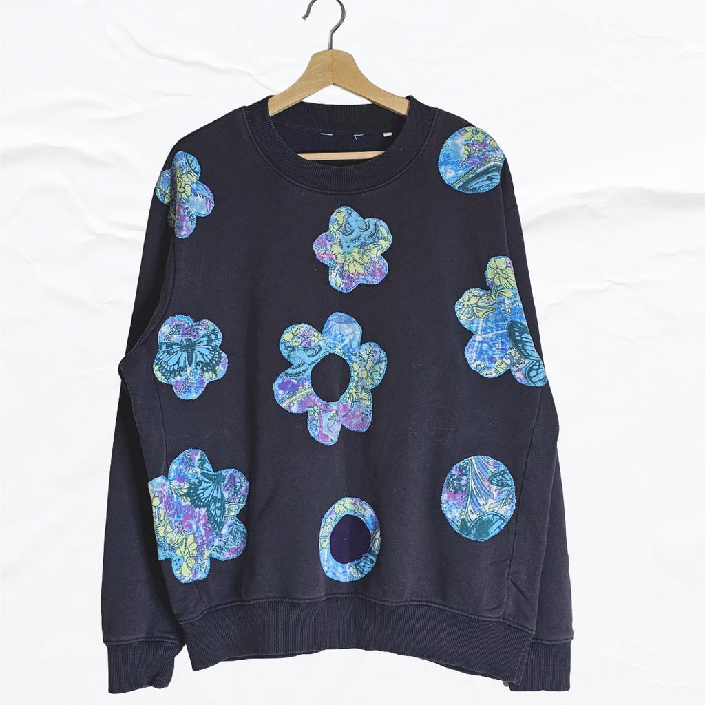 Upcycled black sweatshirt with colorful boho floral appliqué patches on the front.