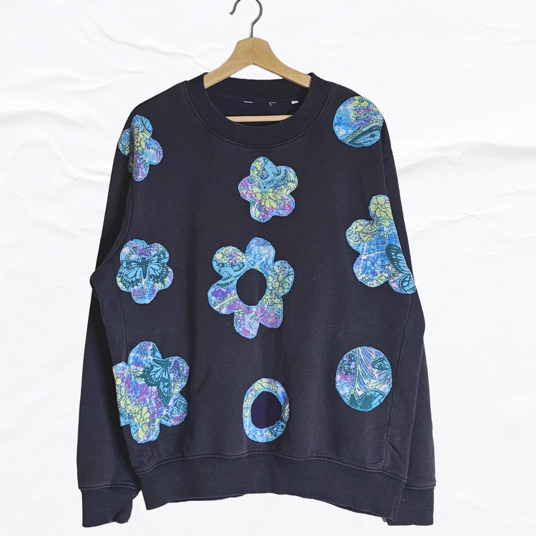 Upcycled black sweatshirt with colorful boho floral appliqué patches on the front.