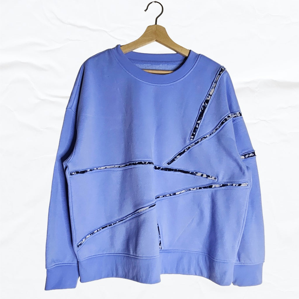 Upcycled periwinkle blue sweatshirt with abstract cut-line patchwork detailing on the front.